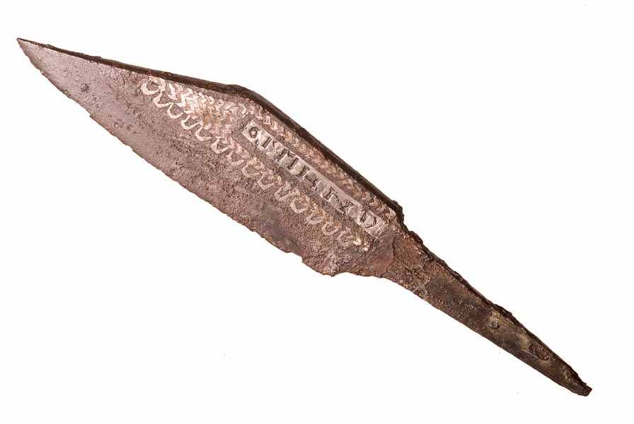 Iron knife. It has inlaid silver decoration of a row of semi-circles, a herringbone pattern and letters of an unreadable word. The handle is missing.
