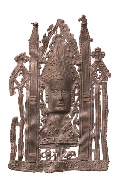 Pewter pilgrim badge of the head of St Thomas Becket wearing a bishop's mitre. Around his head is a church-like architectural frame. Below is an inscription: '+ S CAPVT THOME' (the head of St Thomas).