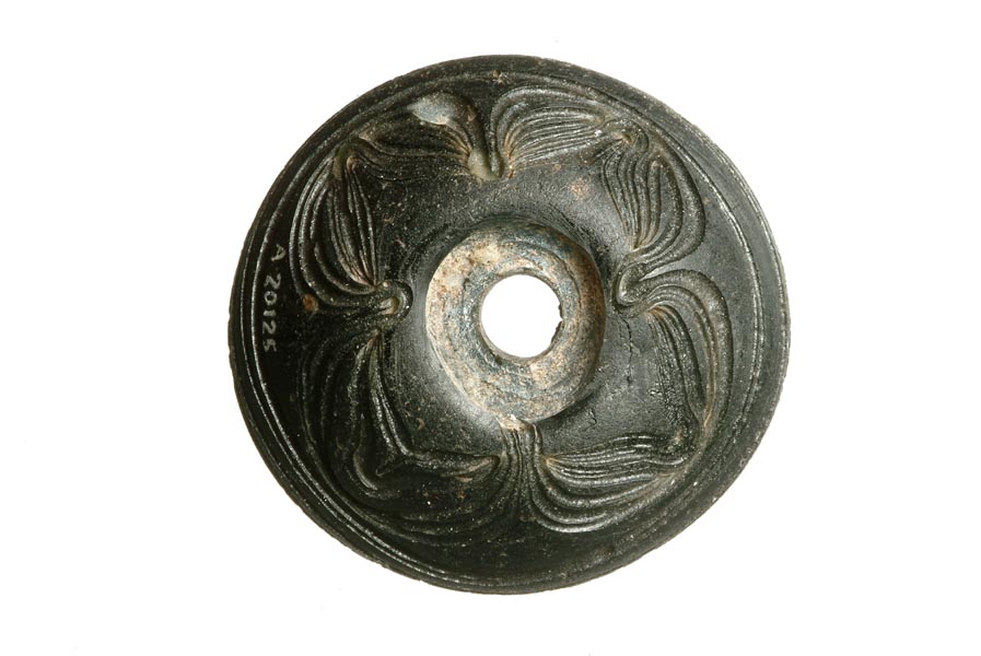 Circular black glass spindle whorl with a hole in the centre for the spindle. It is decorated with 4 swirls on the surface of the glass.