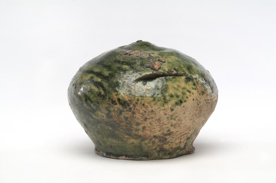 Ceramic money box. It is round, with a slightly pointed top and a flat base. It has a horizontal slot for coins and is glazed a speckly green colour.