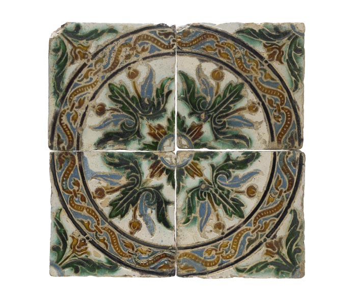 4 square tiles, put together to form a circular pattern with leaves and flowers in the centre. The tiles are white with the decoration in green, blue and brown.