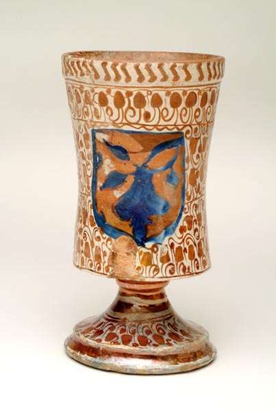 White jug, shaped like a large goblet. It is decorated with copper-coloured vine leaves and scrolls. At the front of the jug is a shield painted blue and copper.