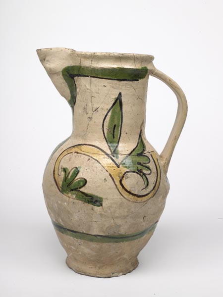 White jug with painted decoration of leaves and branches. The leaves are green, the branch is yellow and their outlines are painted dark brown.