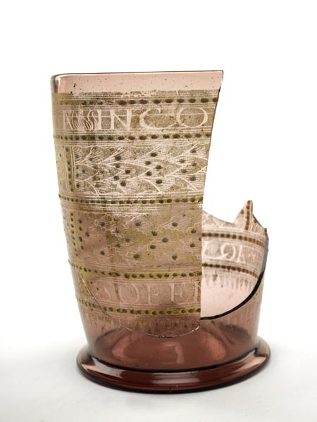 Pale purple glass beaker with gilded decoration of leaves and an inscription. Part of the side is missing.