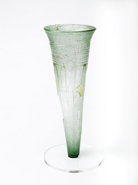 Glass cone beaker with a pointed base, made from pale green glass. It is decorated with thin trails of glass in a spiral around the neck and in long loops down the body.