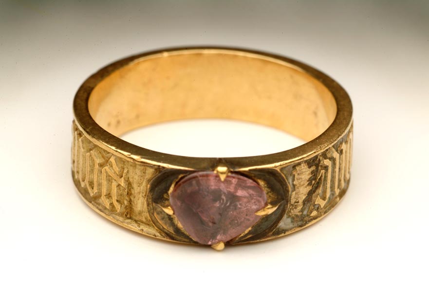 Gold ring, set with a purple spinel in a claw setting. There is an inscription around the sides.