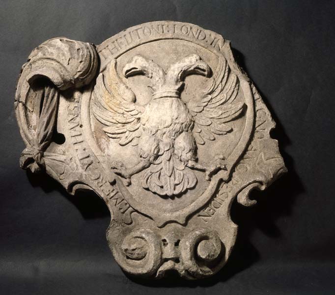 Stone plaque with a double-headed eagle in the centre (the arms of the Hanseatic League). Around the edge is an inscription: 'SI:MERCAT:HANSE:THEUTONI;LOND:IN REGNO:ANG:RESIDEN'.