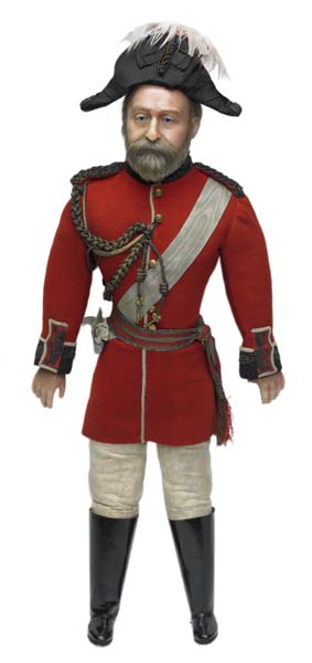 Wax doll of Edward VII dressed in uniform.  He wears a red jacket with a white sash, white trousers, black boots and a black hat with a white plume.