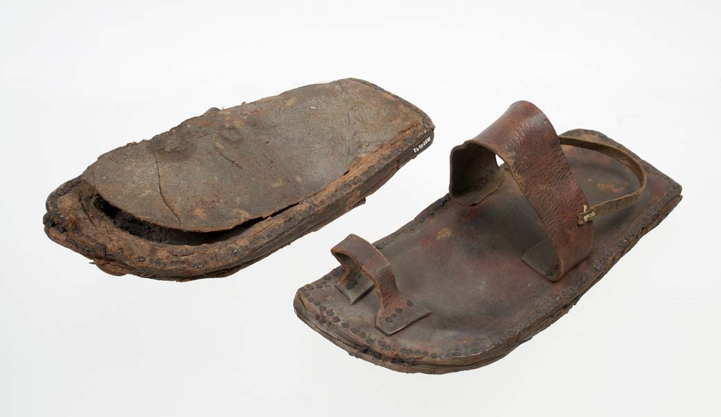 Leather sandals with foot, ankle and toe straps.  One sandal is upside down to show the sole detached from the base.