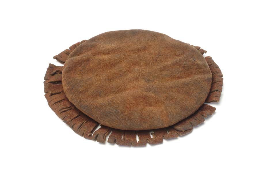 Boy's circular knitted cap with a brim decorated with slashes. The wool has turned brown with age. There are patches of the felted surface still remaining.