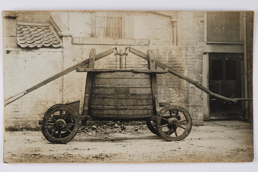 Photograph: fire engine. Oval wooden barrel with metal pipe in the centre. The pumping arms and wheels are missing.