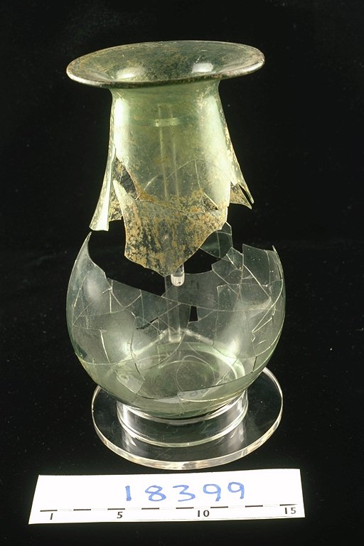 Urinal flask, of pale green glass with flared neck and rounded base. It is made from many fragments stuck together.